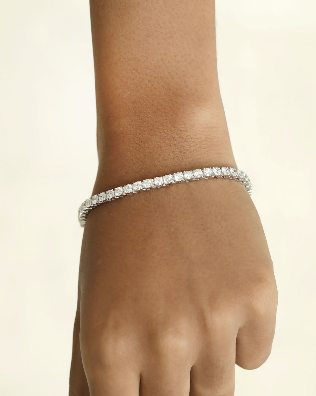Diamond bracelet on a wrist against a beige background