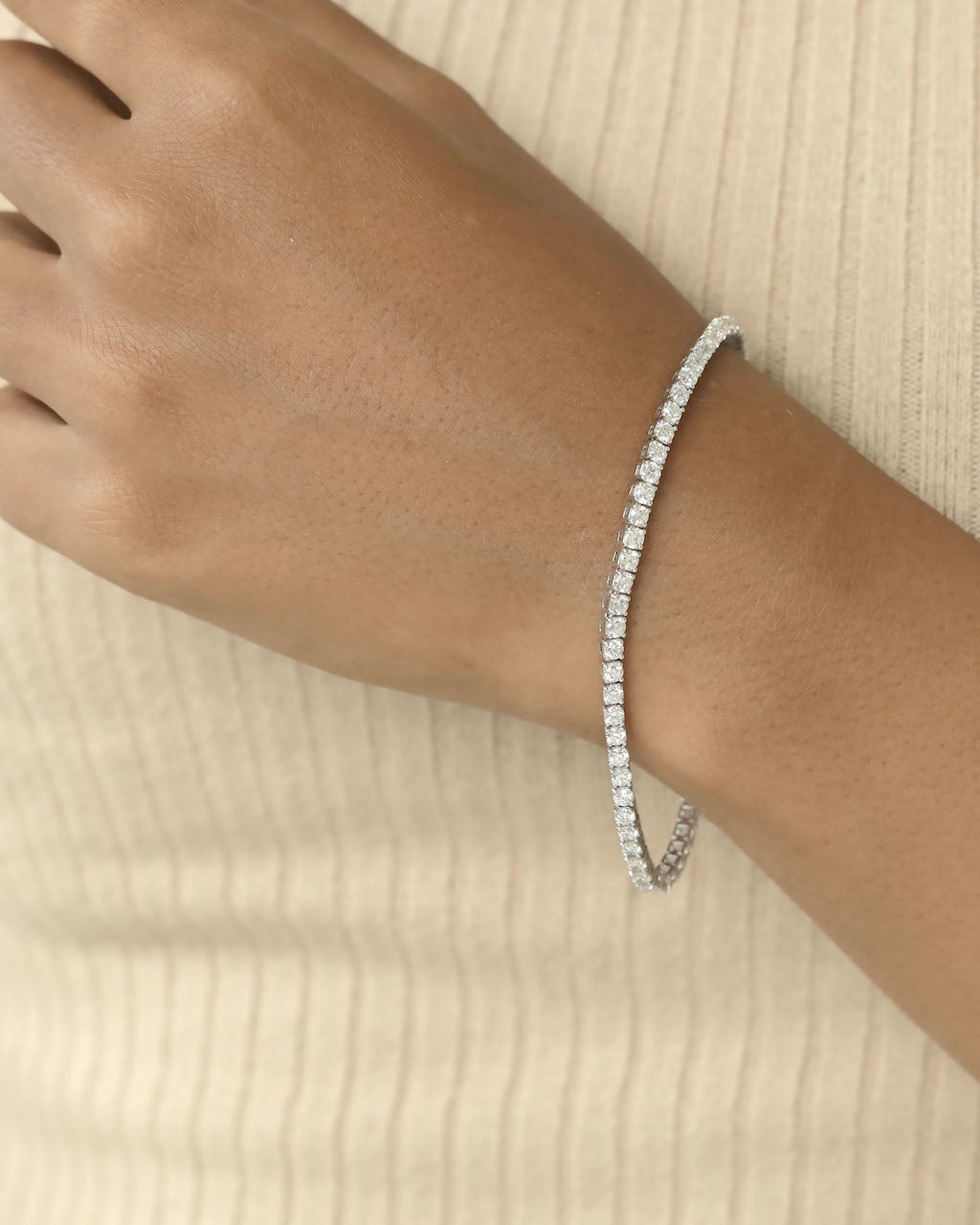 Diamond bracelet on a wrist against a beige background
