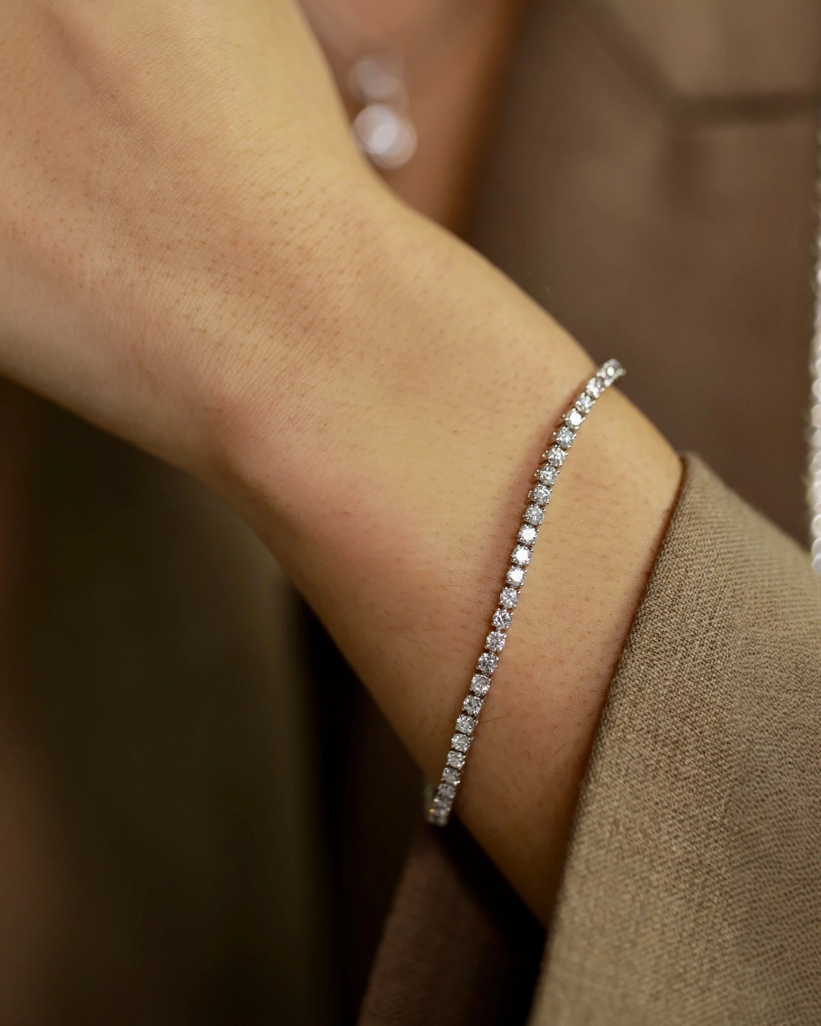 Diamond bracelet on a wrist against a beige background
