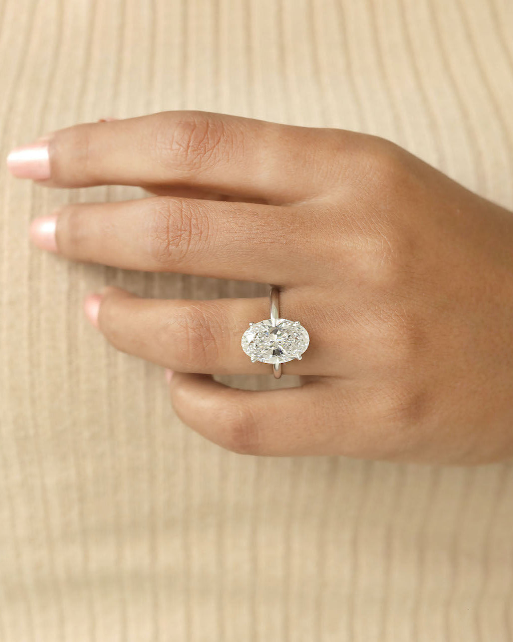 Hand wearing a diamond ring on a beige background