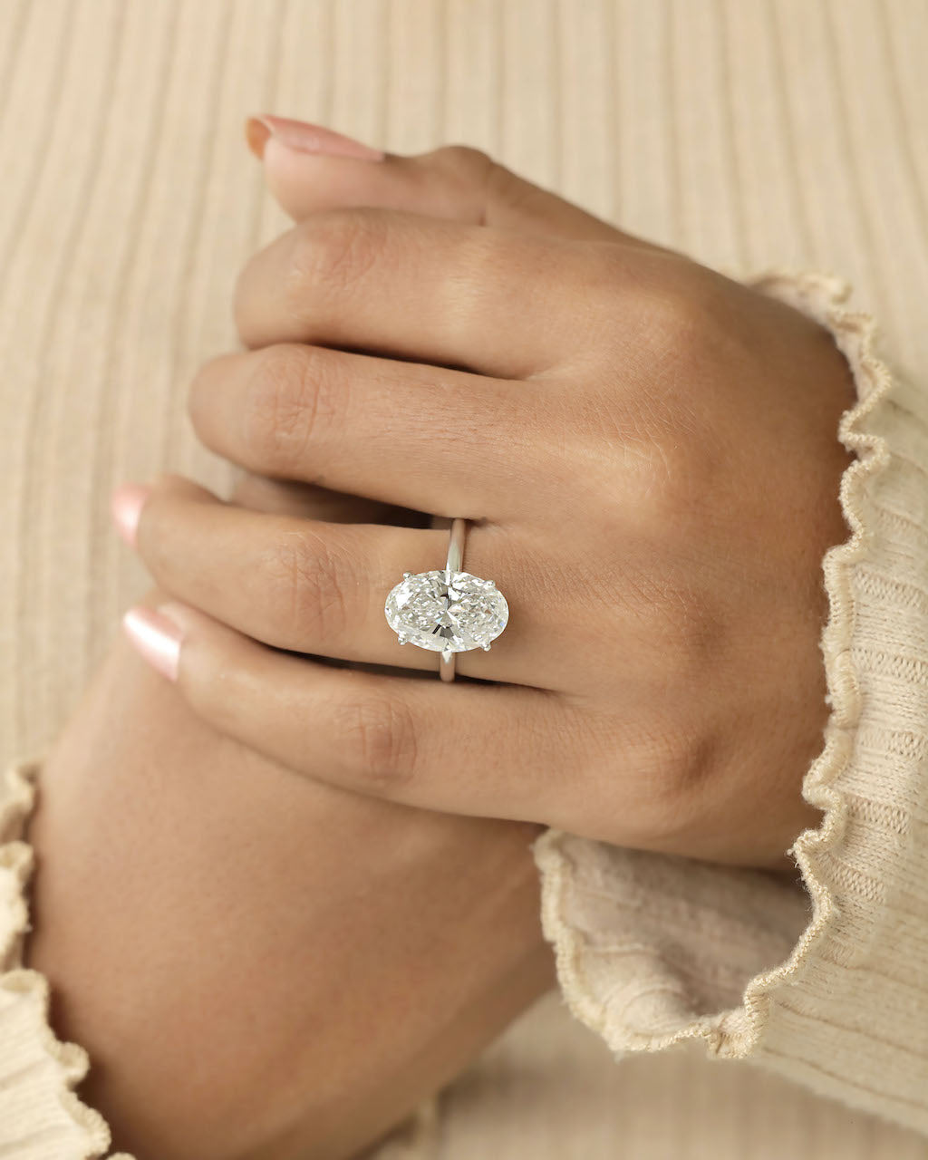 Hand wearing a diamond ring with a beige background