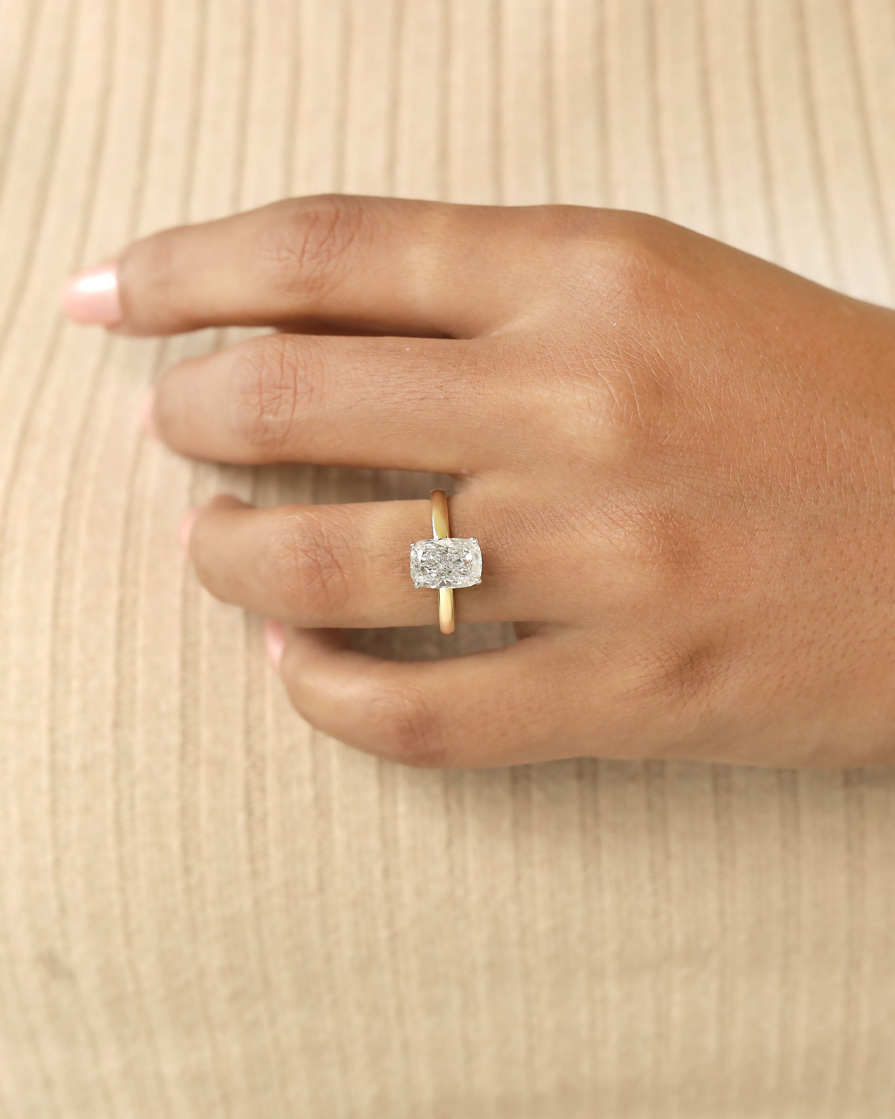 Hand wearing a diamond ring on a beige background.
