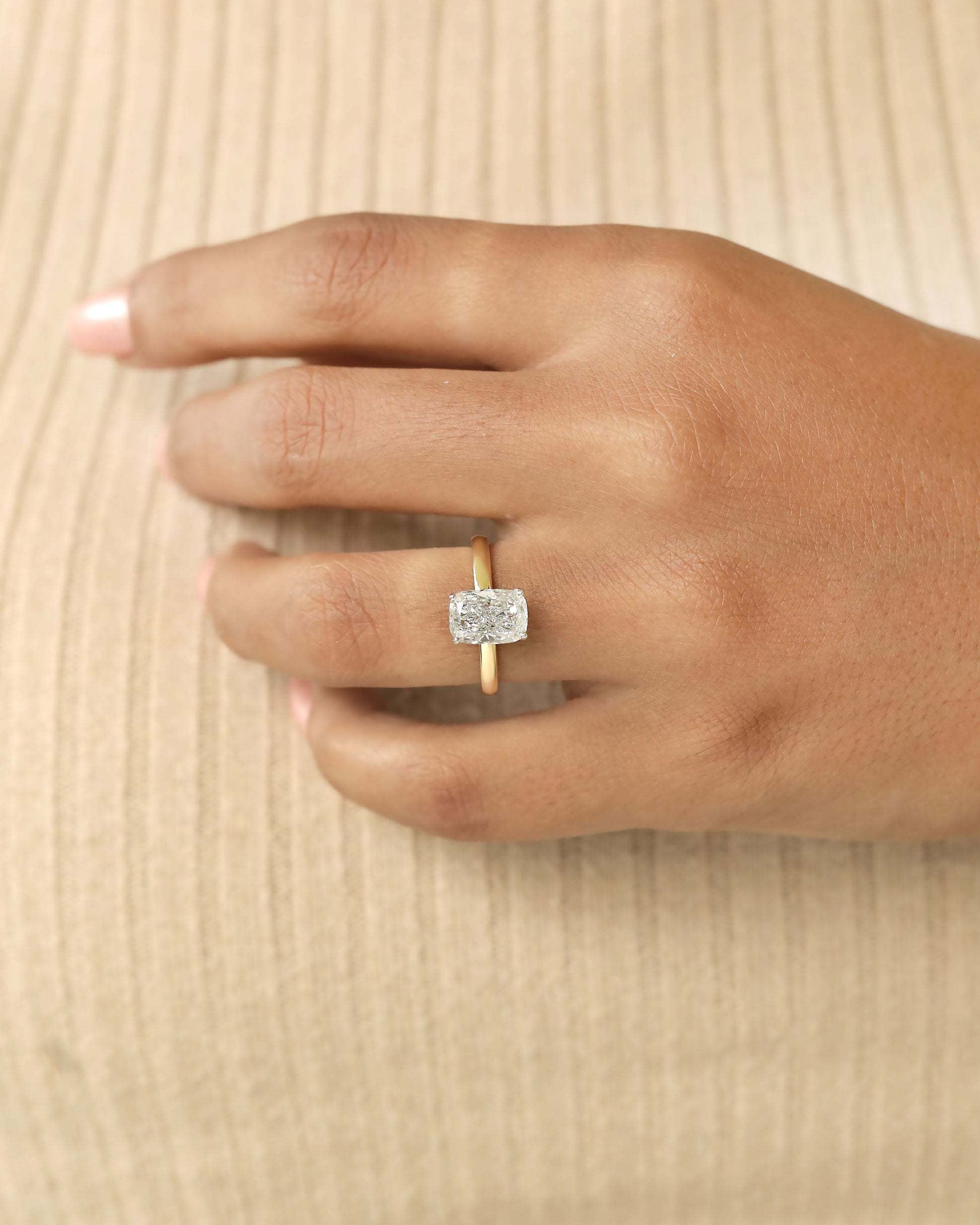 Hand wearing a diamond ring on a beige background.