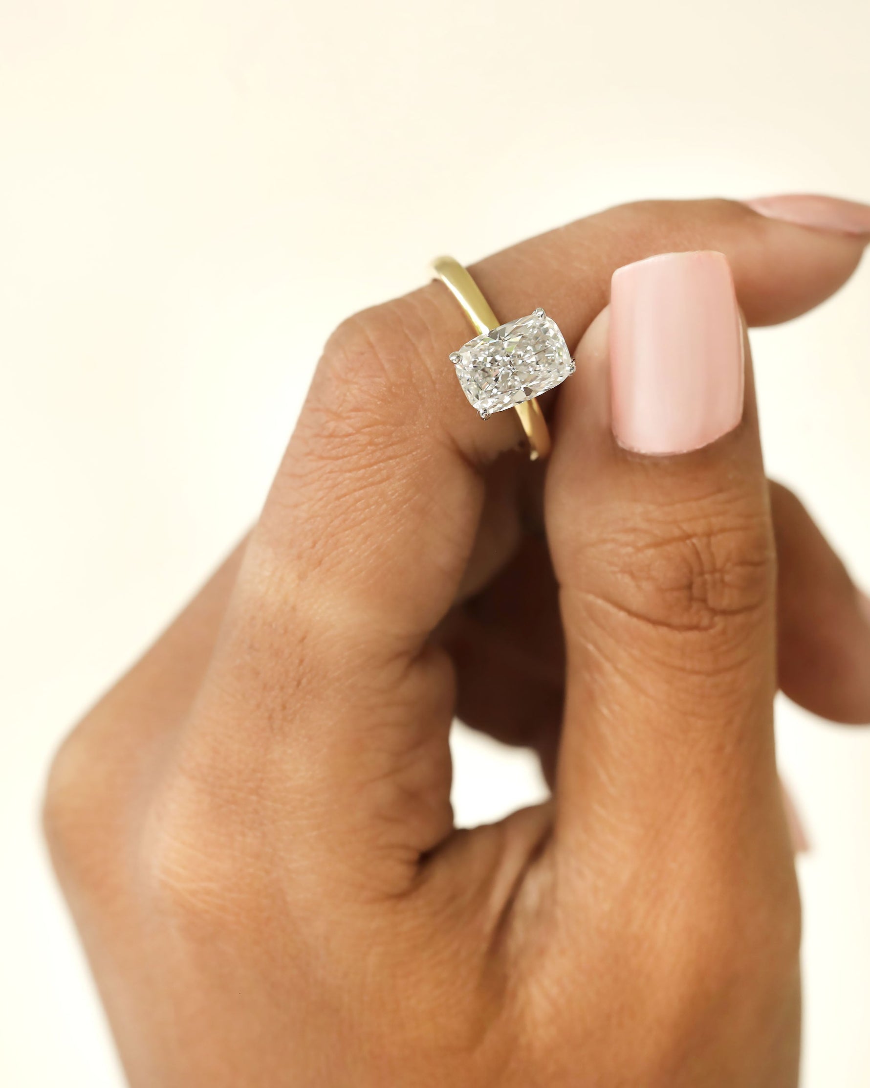 Hand holding a diamond ring on a beige background.