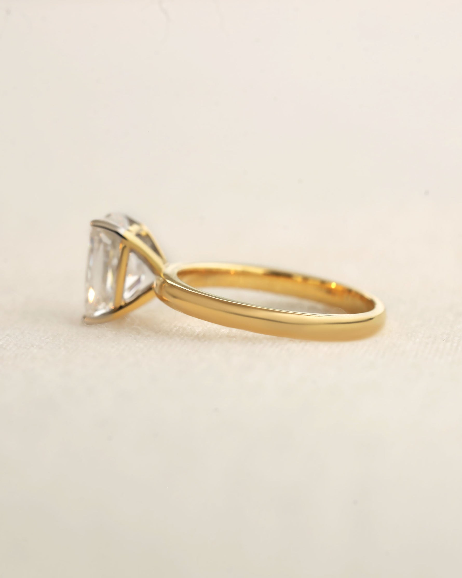 Gold ring with a large diamond on a beige background.