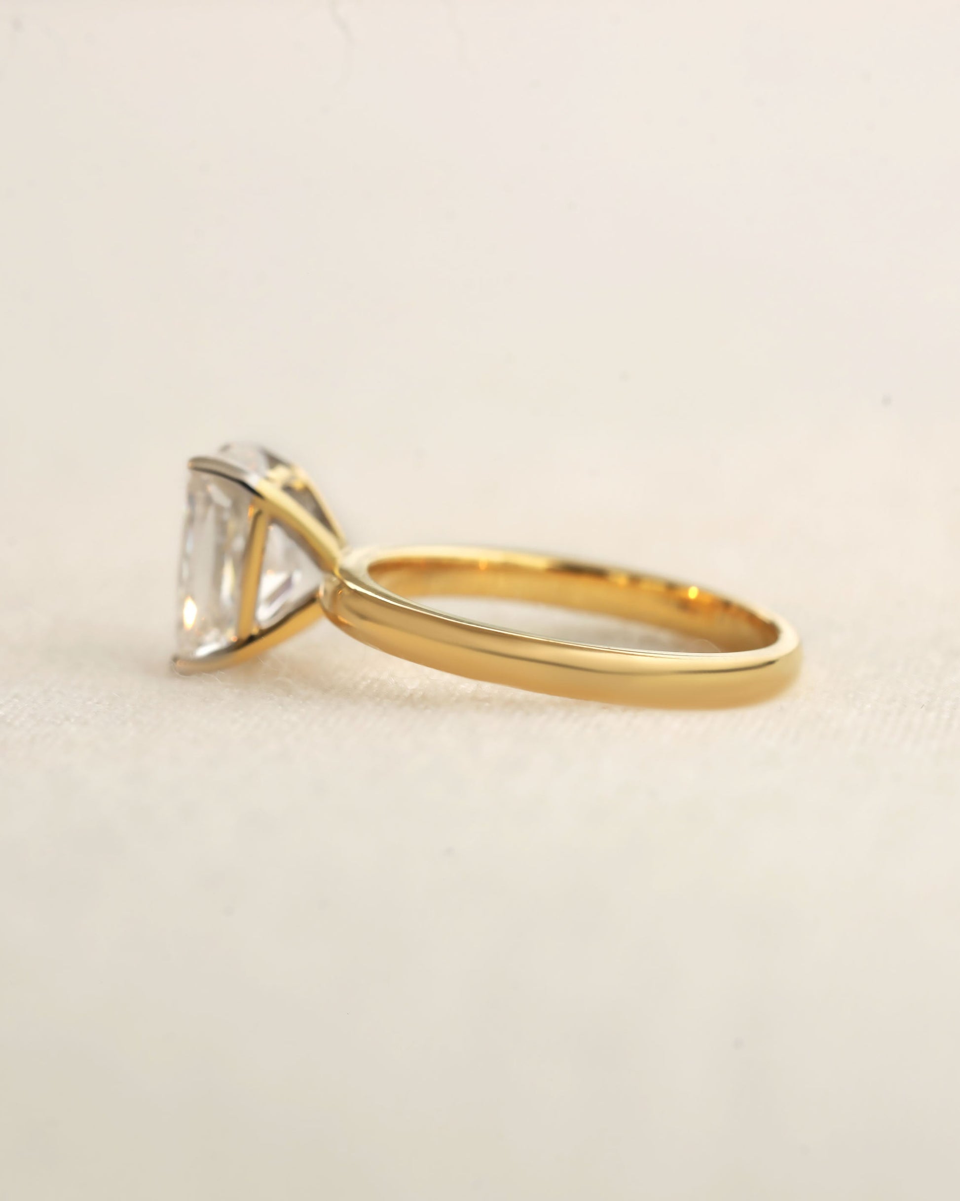 Gold ring with a large diamond on a beige background.
