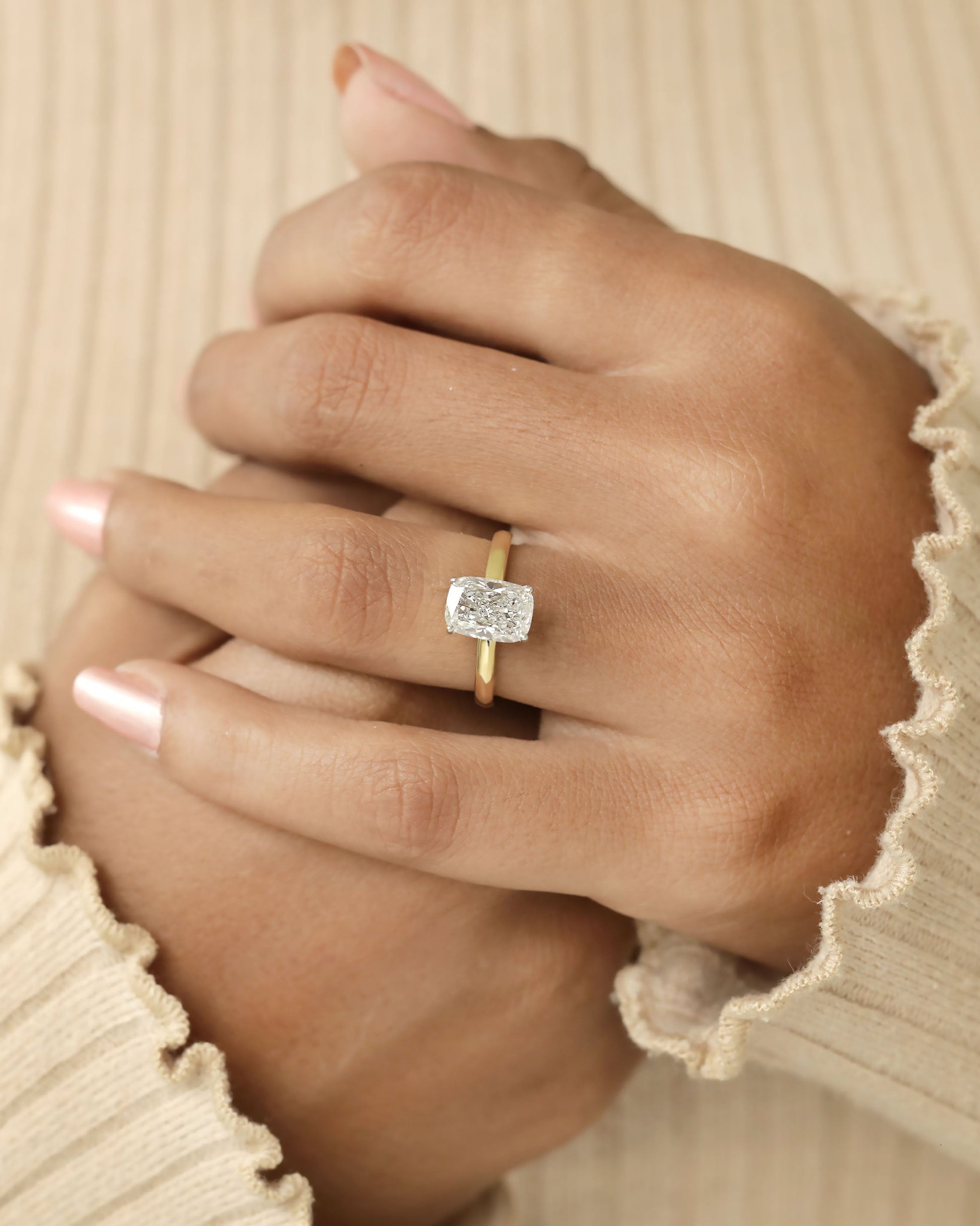 Hand wearing a diamond ring on a beige background.