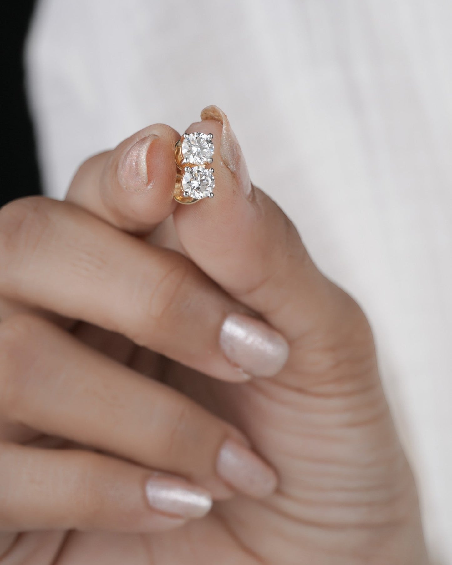 Hand holding diamond studs earrings in yellow gold.