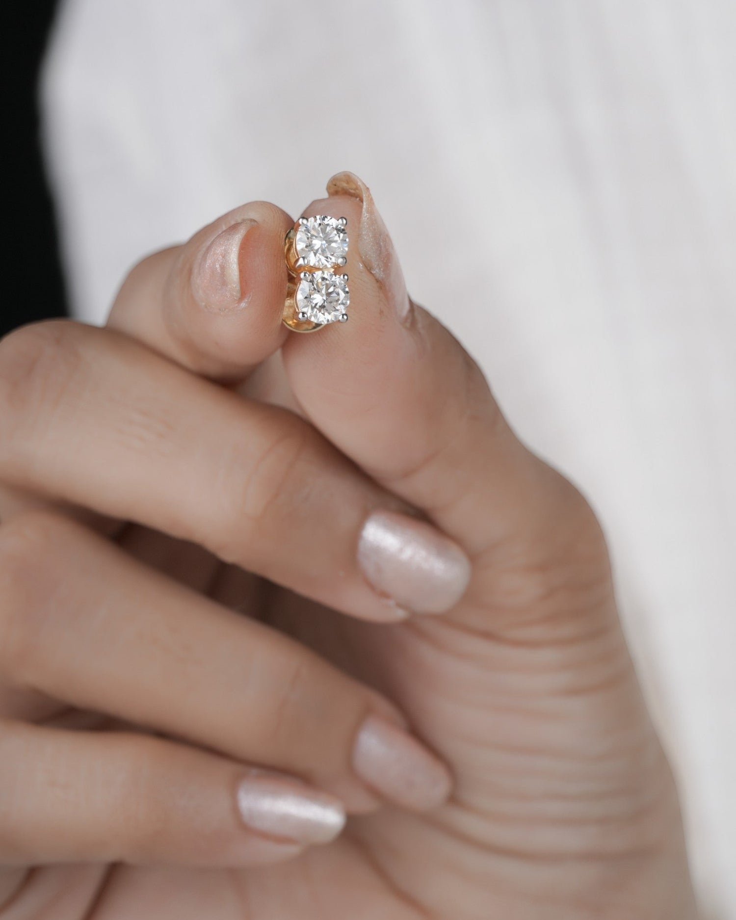 Hand holding diamond studs earrings in yellow gold.