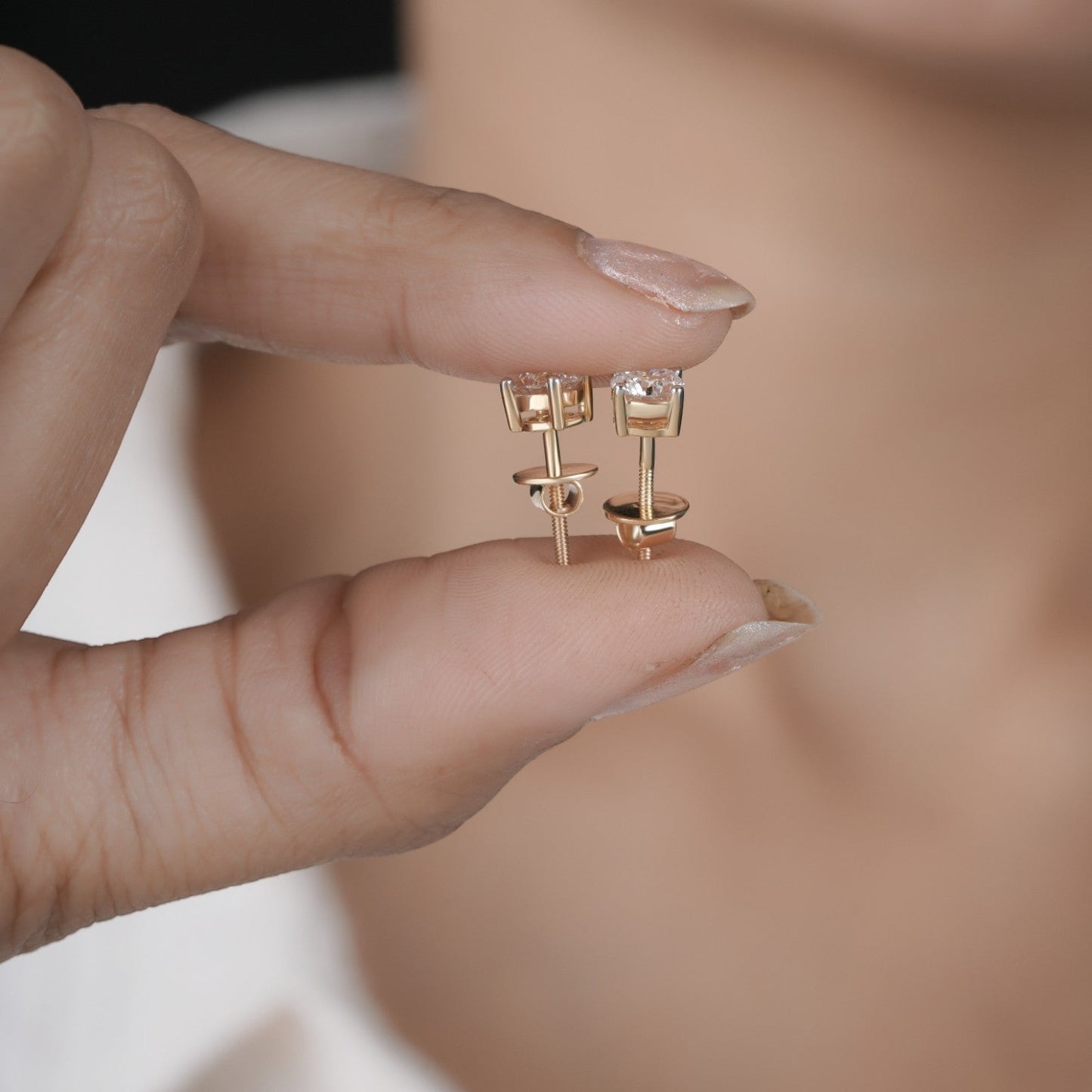 Hand holding diamond studs earrings in yellow gold.