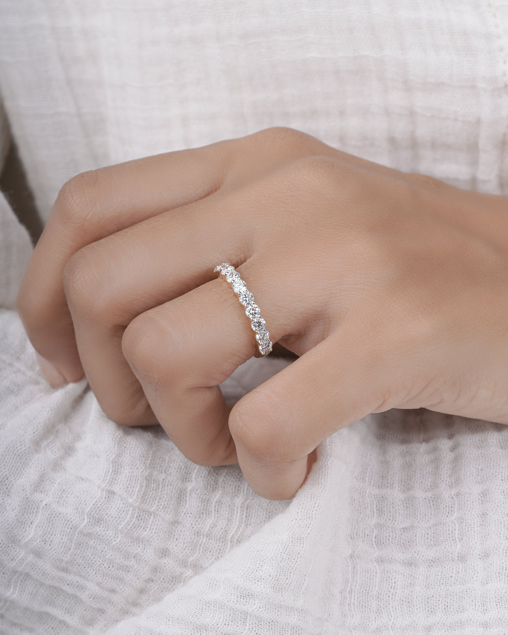 Half eternity ring on a person's finger against a neutral background.