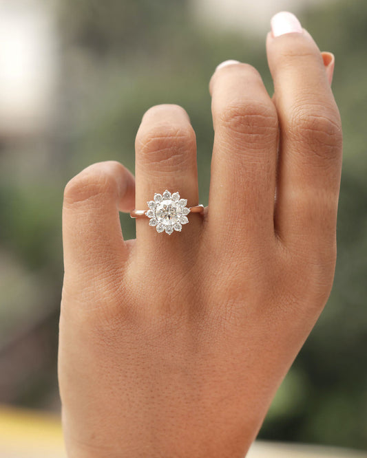 Hand wearing a diamond ring with a blurred natural background.