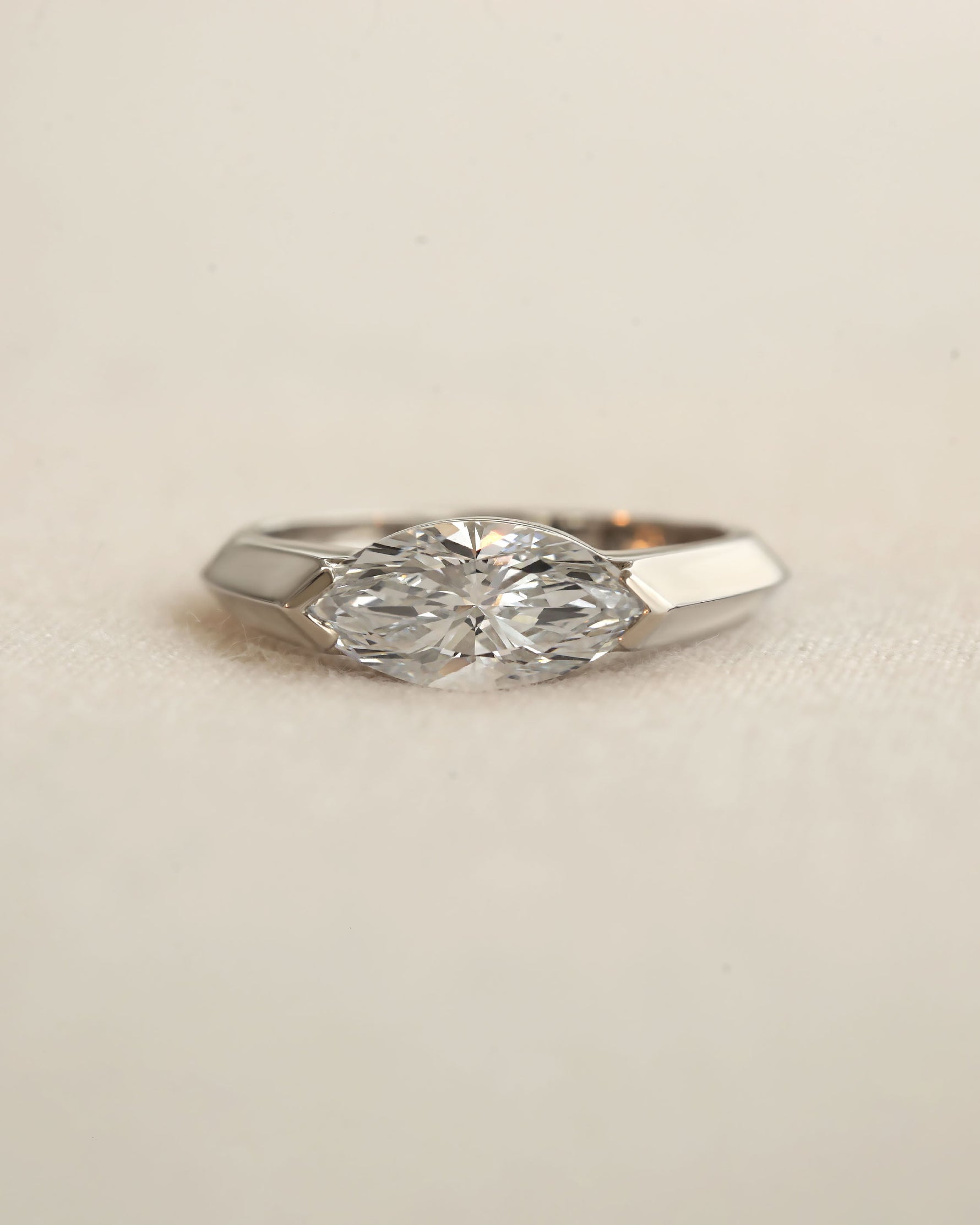 Marquise cut diamond bezel ring in white gold on white background.