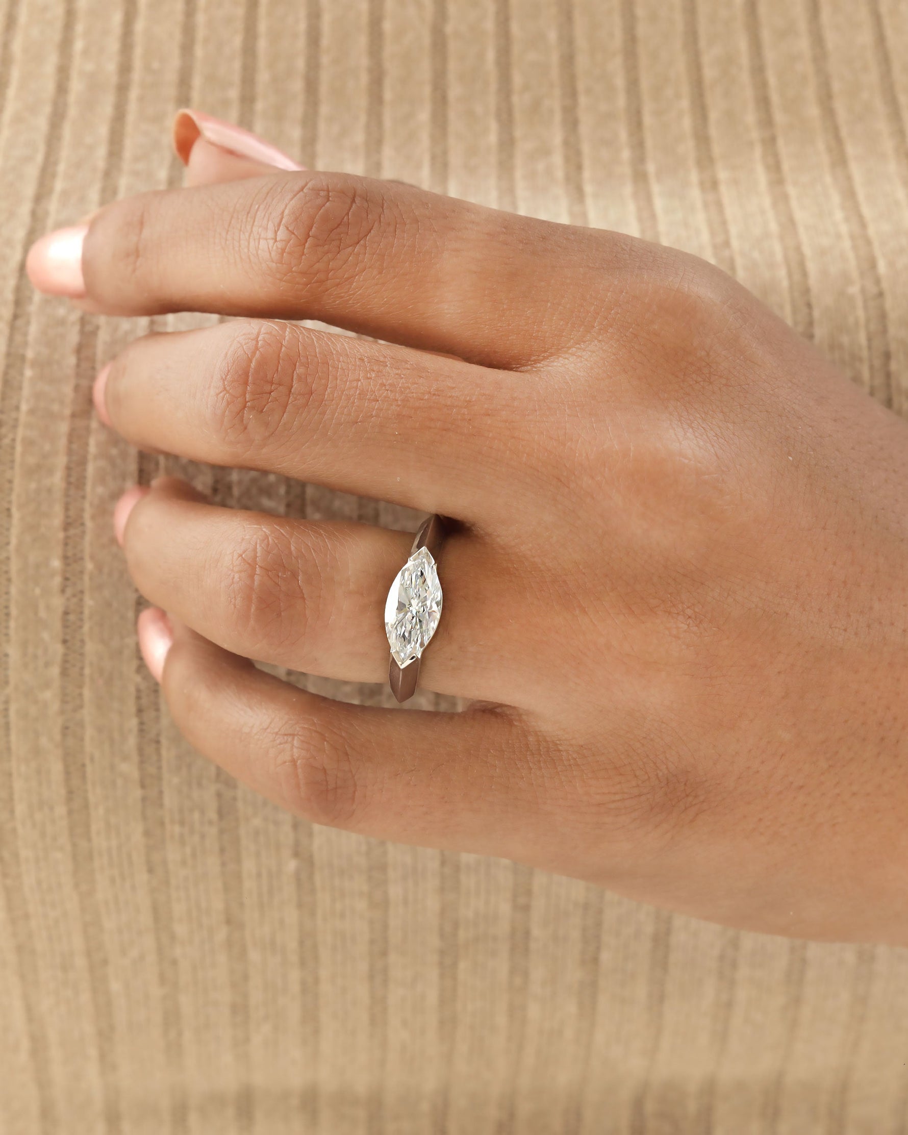 Hand wearing a marquise cut diamond bezel ring in white gold.