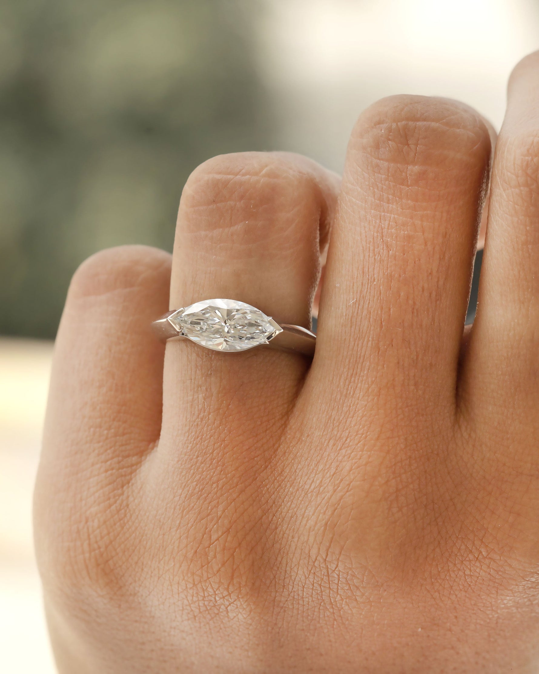 Hand wearing a marquise cut diamond bezel ring in white gold.