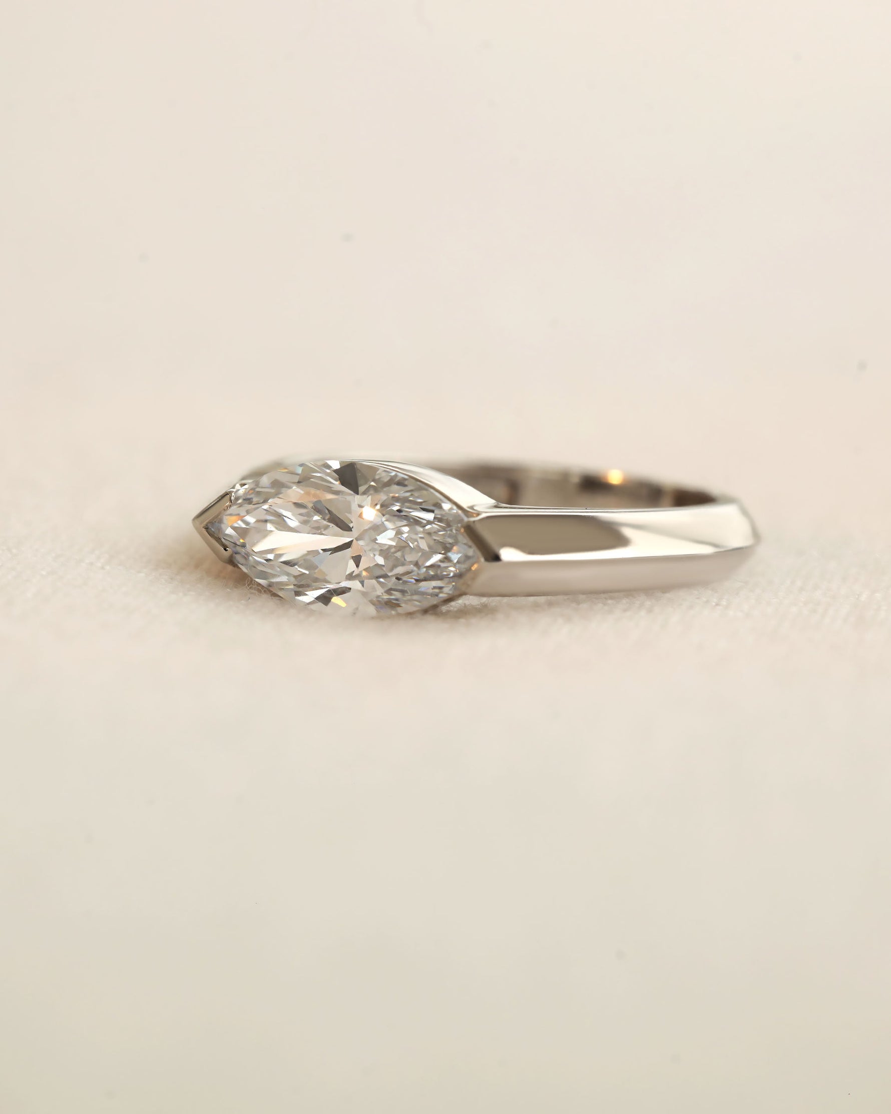 Marquise cut diamond bezel ring in white gold on white background.