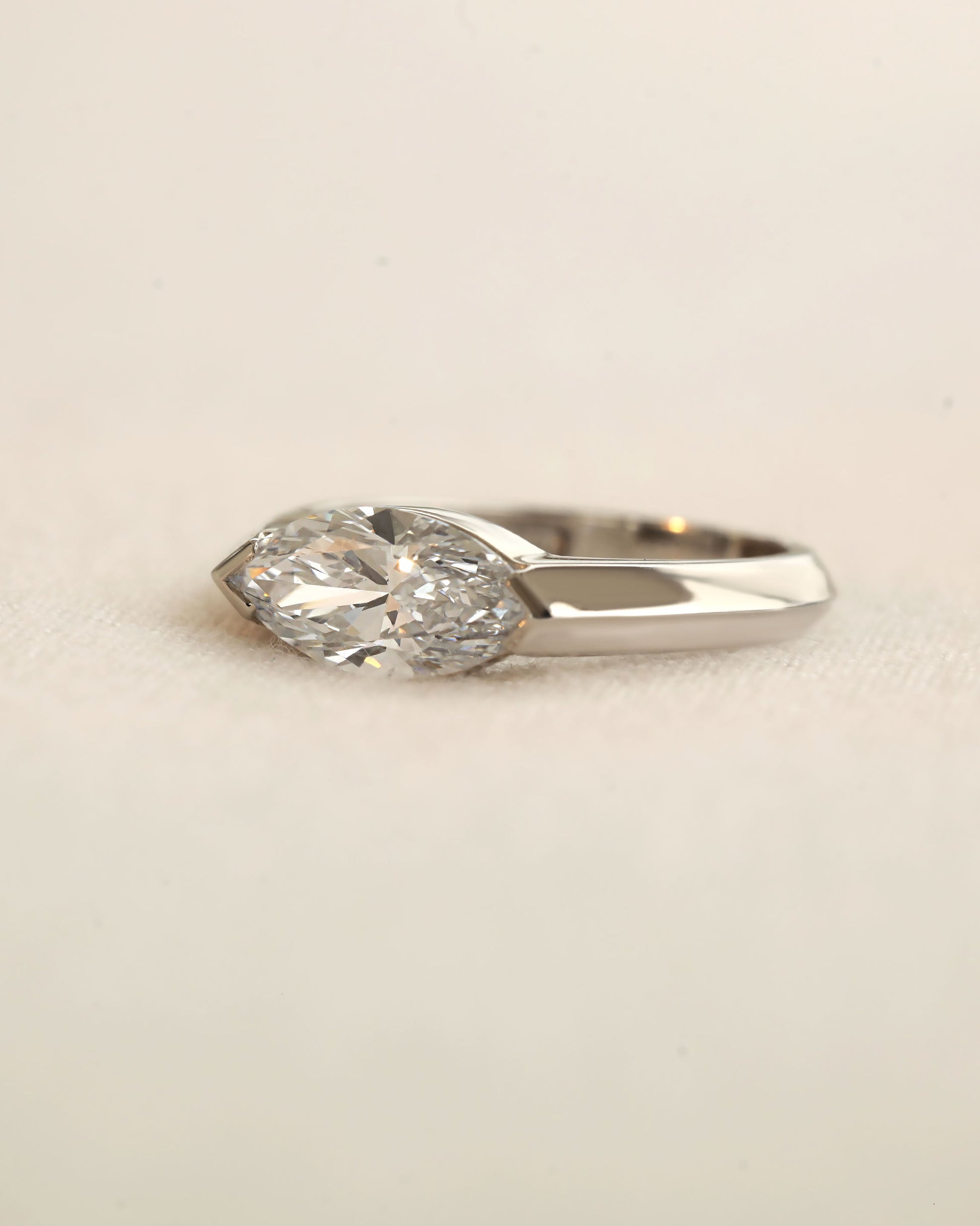 Marquise cut diamond bezel ring in white gold on white background.