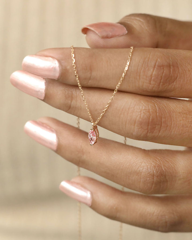 Hand holding marquise cut lab diamond solitaire pendant necklace in yellow gold.