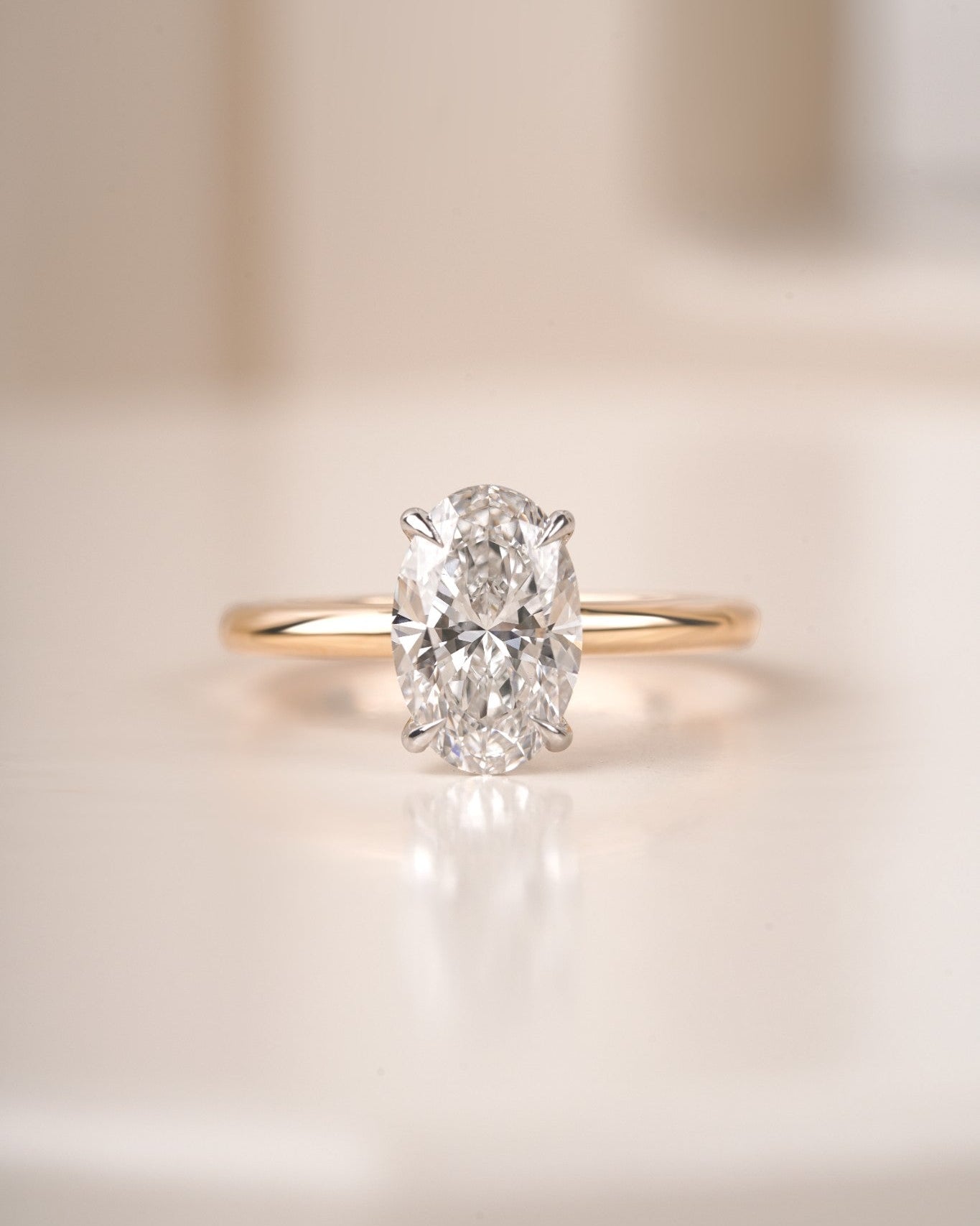 Oval diamond engagement ring in yellow gold on a blur white background.