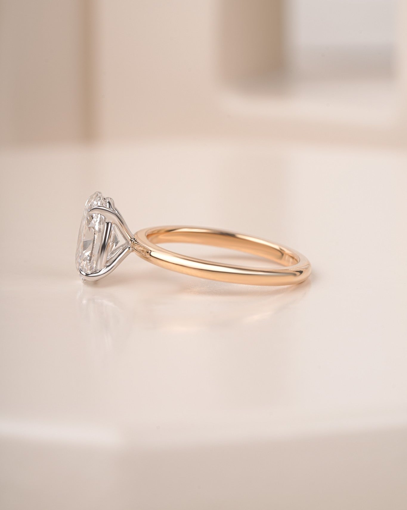 Oval diamond engagement ring in yellow gold on a blur white background.
