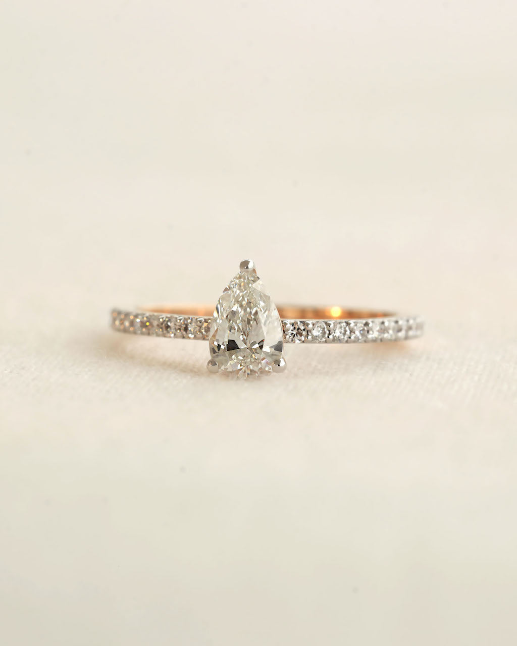 Pear cut lab-grown diamond ring on a light textured background.
