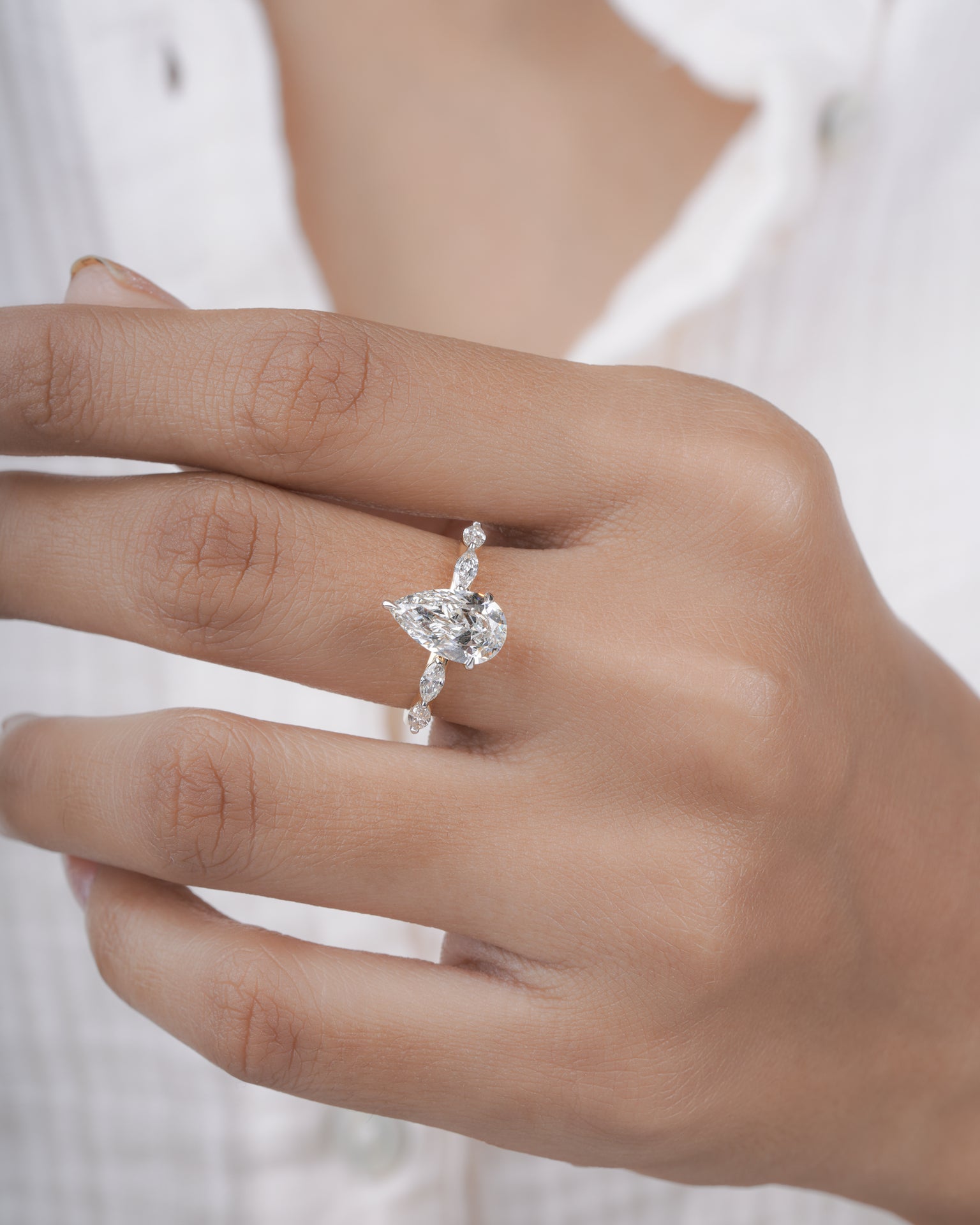 Diamond ring with pear-shaped center stone on a hand.