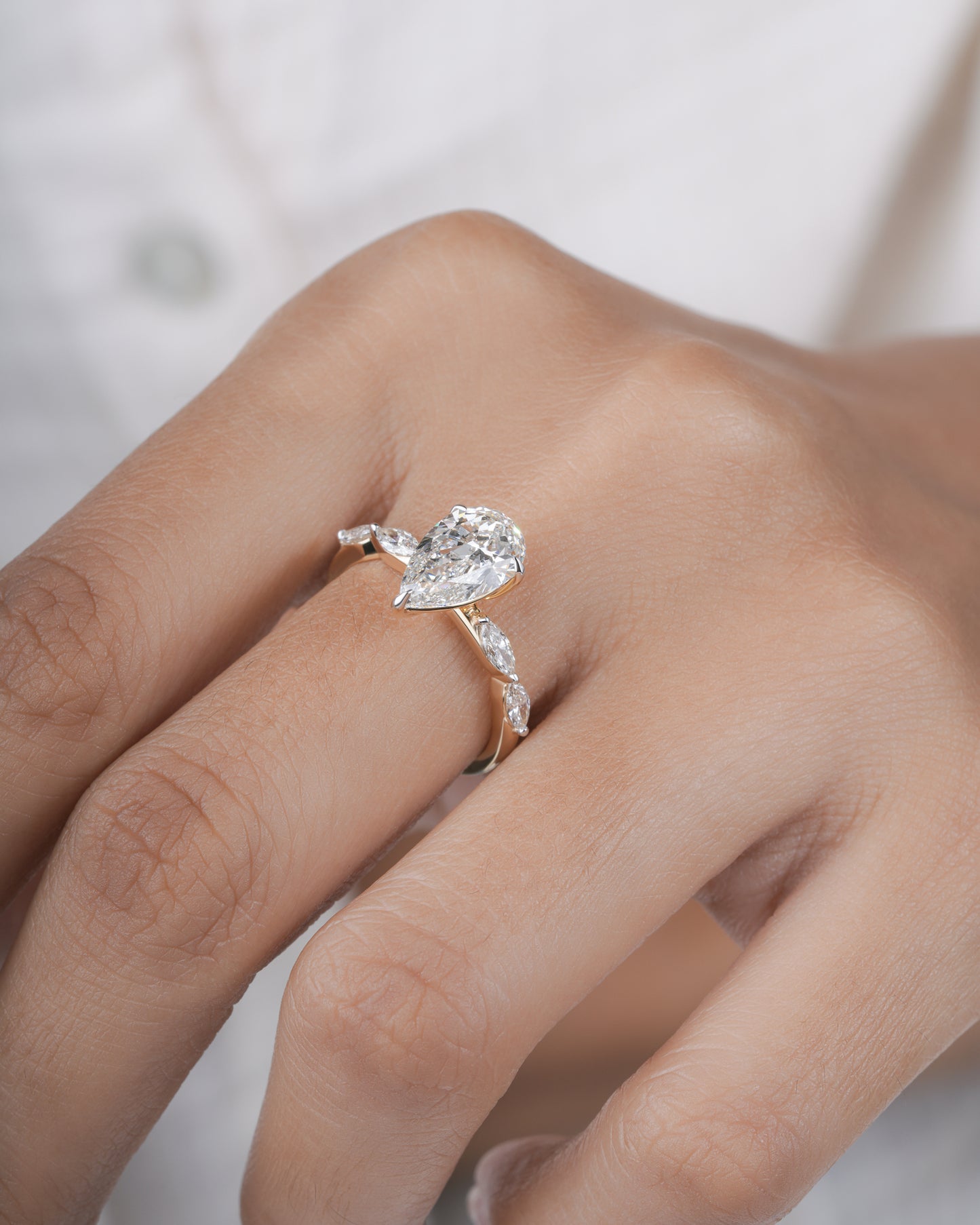 Gold ring with a pear-shaped diamond on a hand.