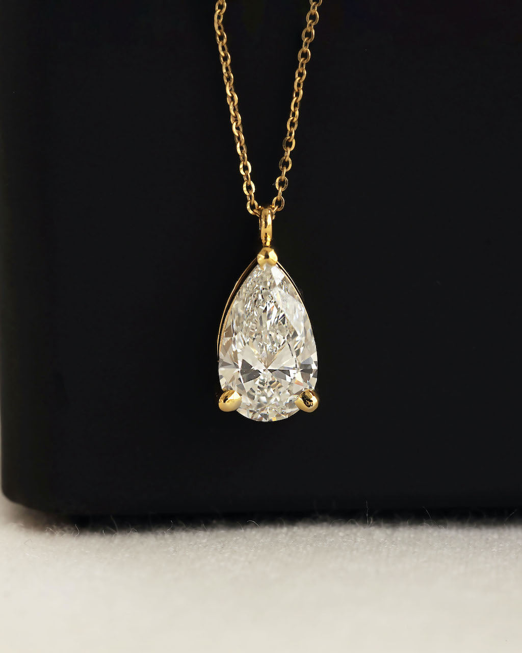 Close up shot of a pear cut lab diamond solitaire pendant necklace in yellow gold aganist a black background.