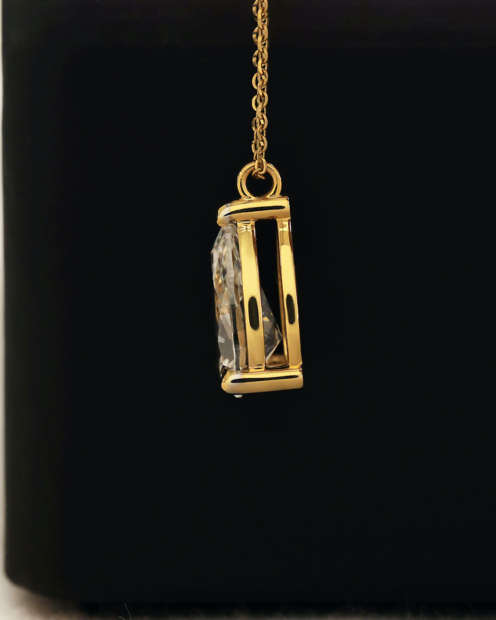 Side view of a pear cut lab diamond solitaire pendant necklace in yellow gold.