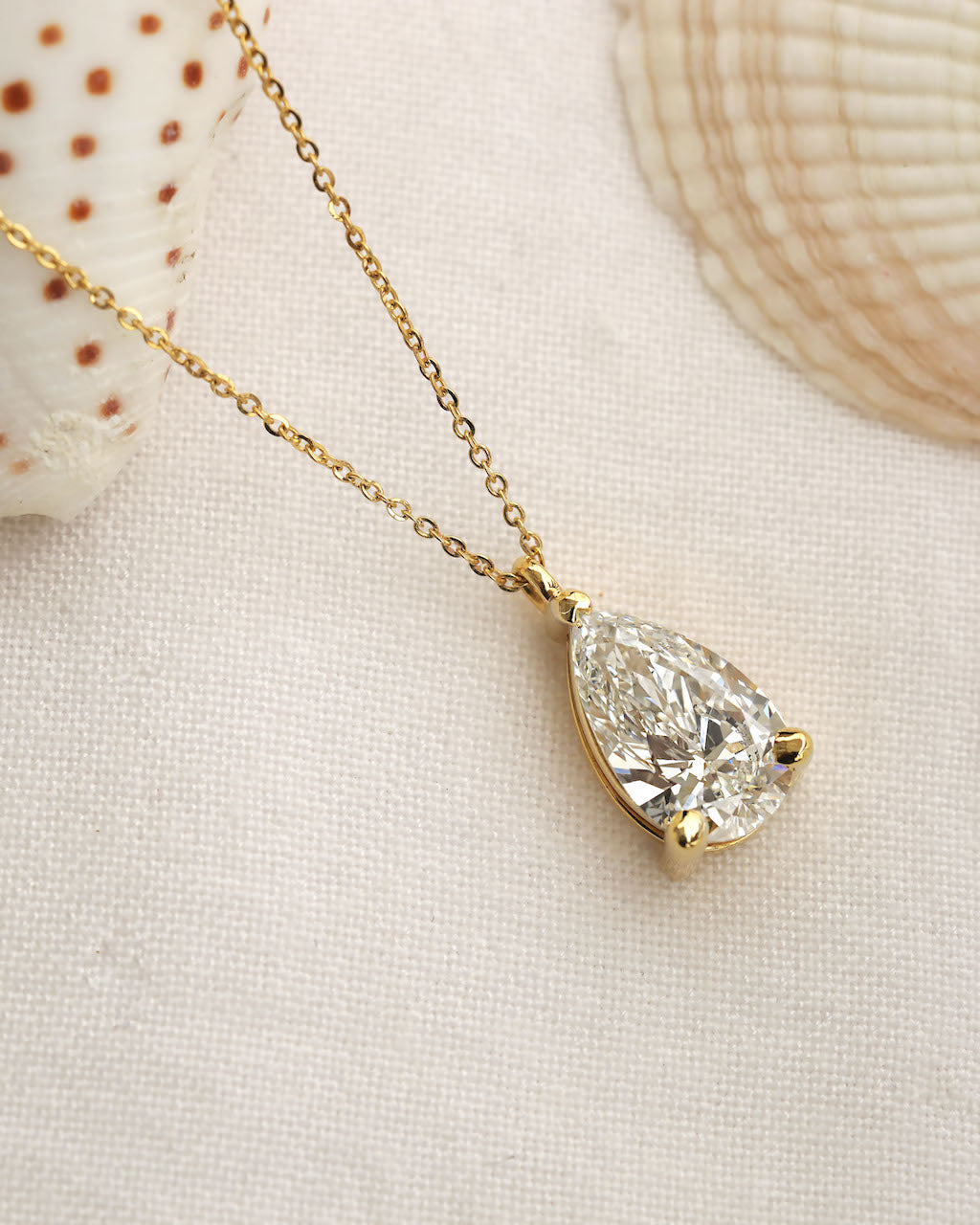 Close up shot of a pear cut lab diamond solitaire pendant necklace in yellow gold.