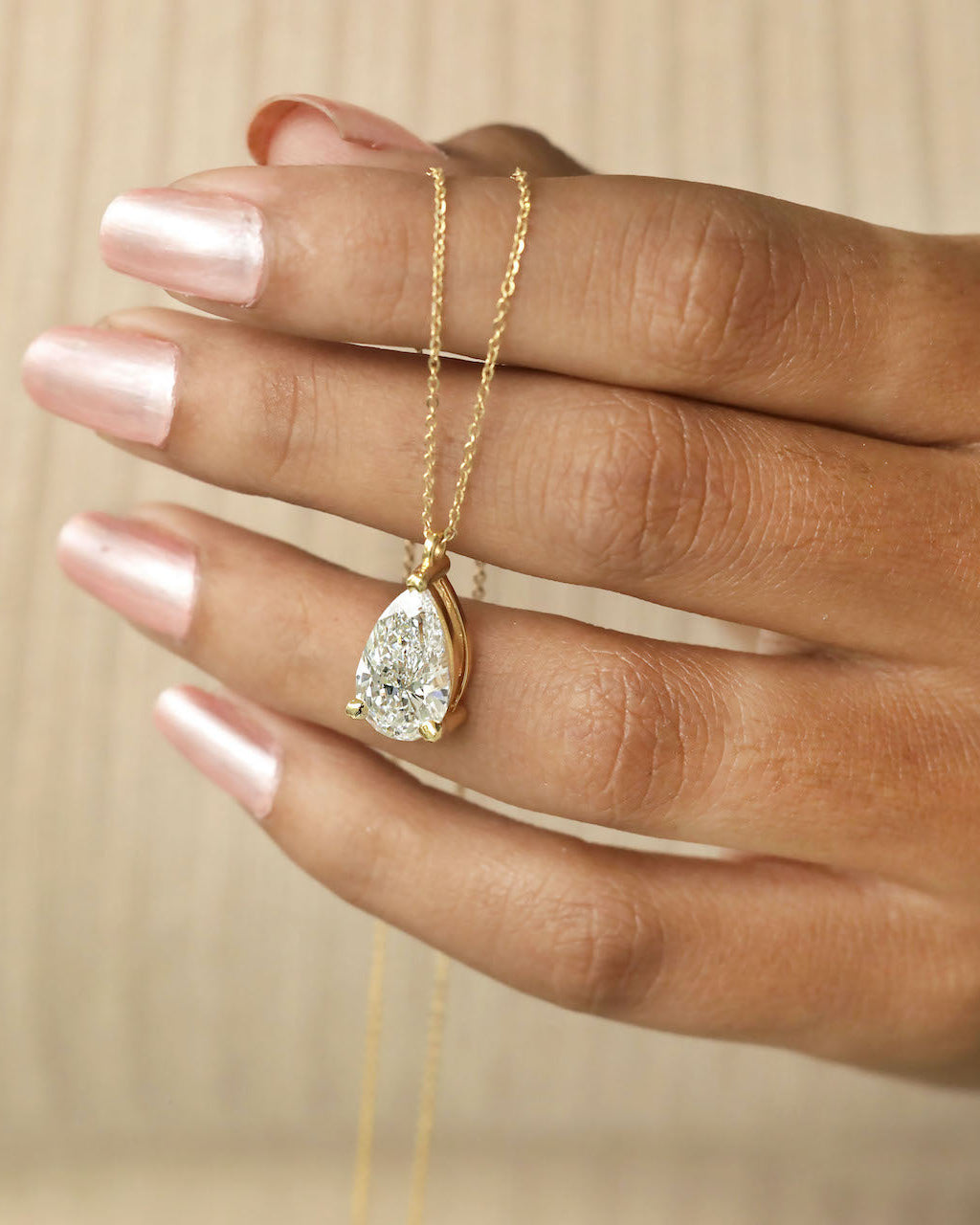 Hand holding a pear cut lab diamond solitaire pendant necklace in yellow gold .