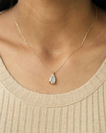 Close up shot of a person wearing pear cut lab diamond solitaire pendant necklace in yellow gold.