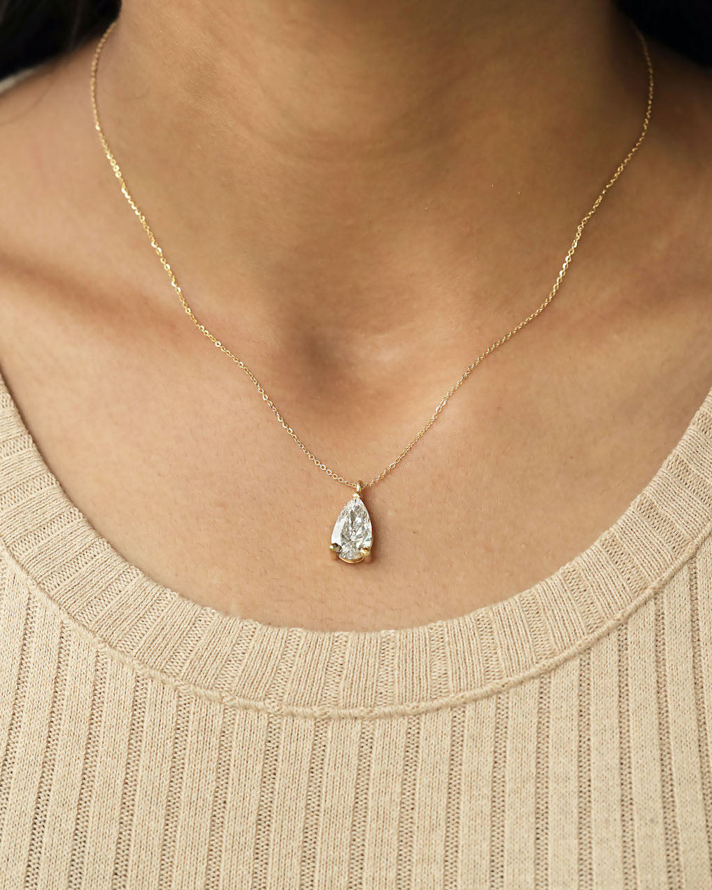 Close up shot of a person wearing pear cut lab diamond solitaire pendant necklace in yellow gold.