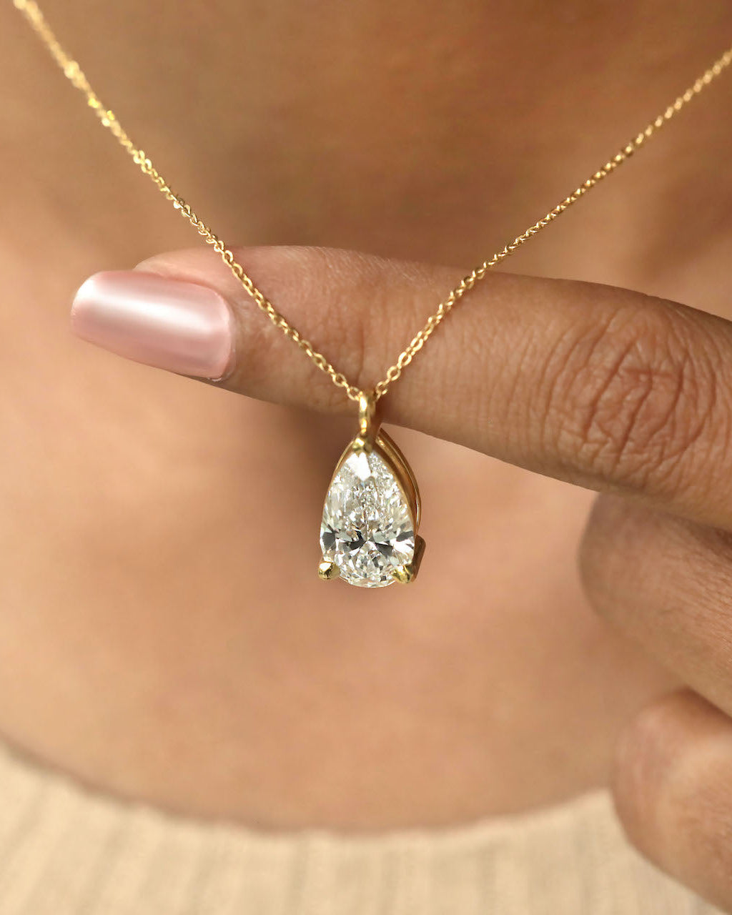 Close up shot of a person wearing pear cut lab diamond solitaire pendant necklace in yellow gold.