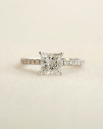 Close up shot of princess cut diamond engagement ring displayed on a white background.