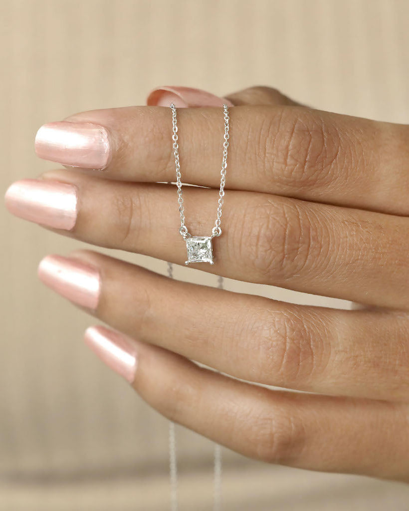 Hand holding princess cut lab diamond solitaire pendant necklace in yellow gold.