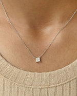 Person wearing princess cut lab diamond solitaire pendant necklace in yellow gold.