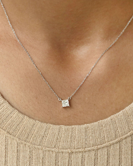 Person wearing princess cut lab diamond solitaire pendant necklace in yellow gold.