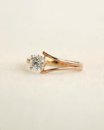 Round cut diamond ring with modern split v band displayed on a light coloured surface. 