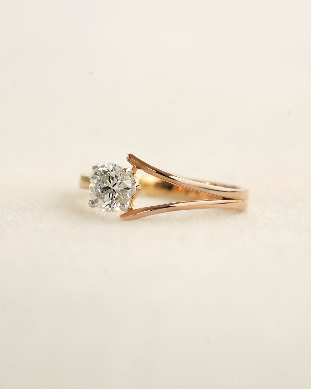 Round cut diamond ring with modern split v band displayed on a light coloured surface. 