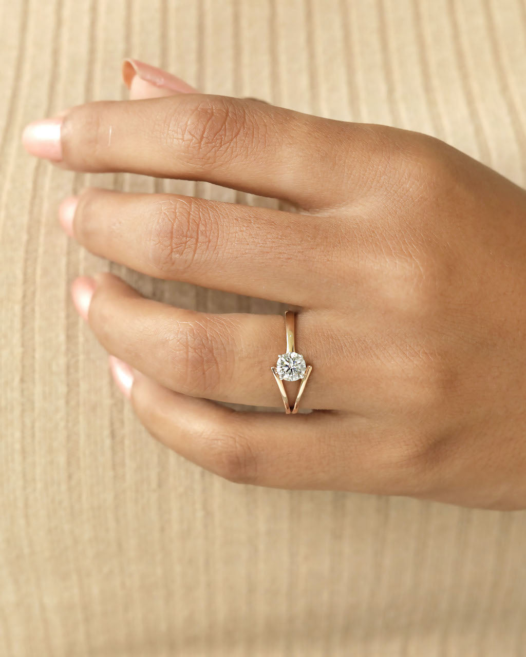 Hand wearing round cut diamond ring with modern split v band in yellow & rose gold.
