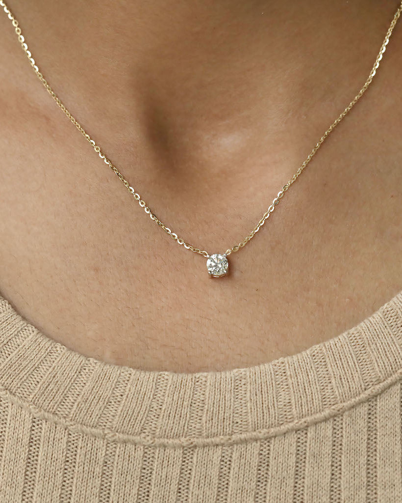 Person wearing round cut lab diamond solitaire pendant necklace in yellow gold.
  