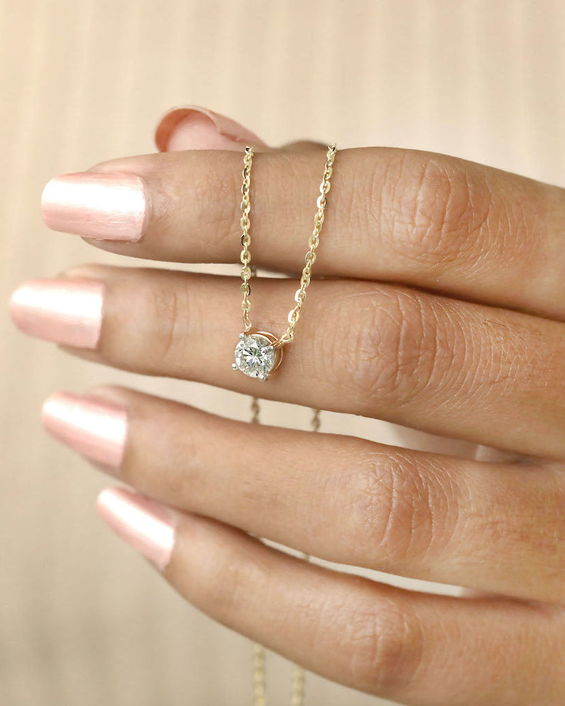 Hand holding round cut lab diamond solitaire pendant necklace in yellow gold.