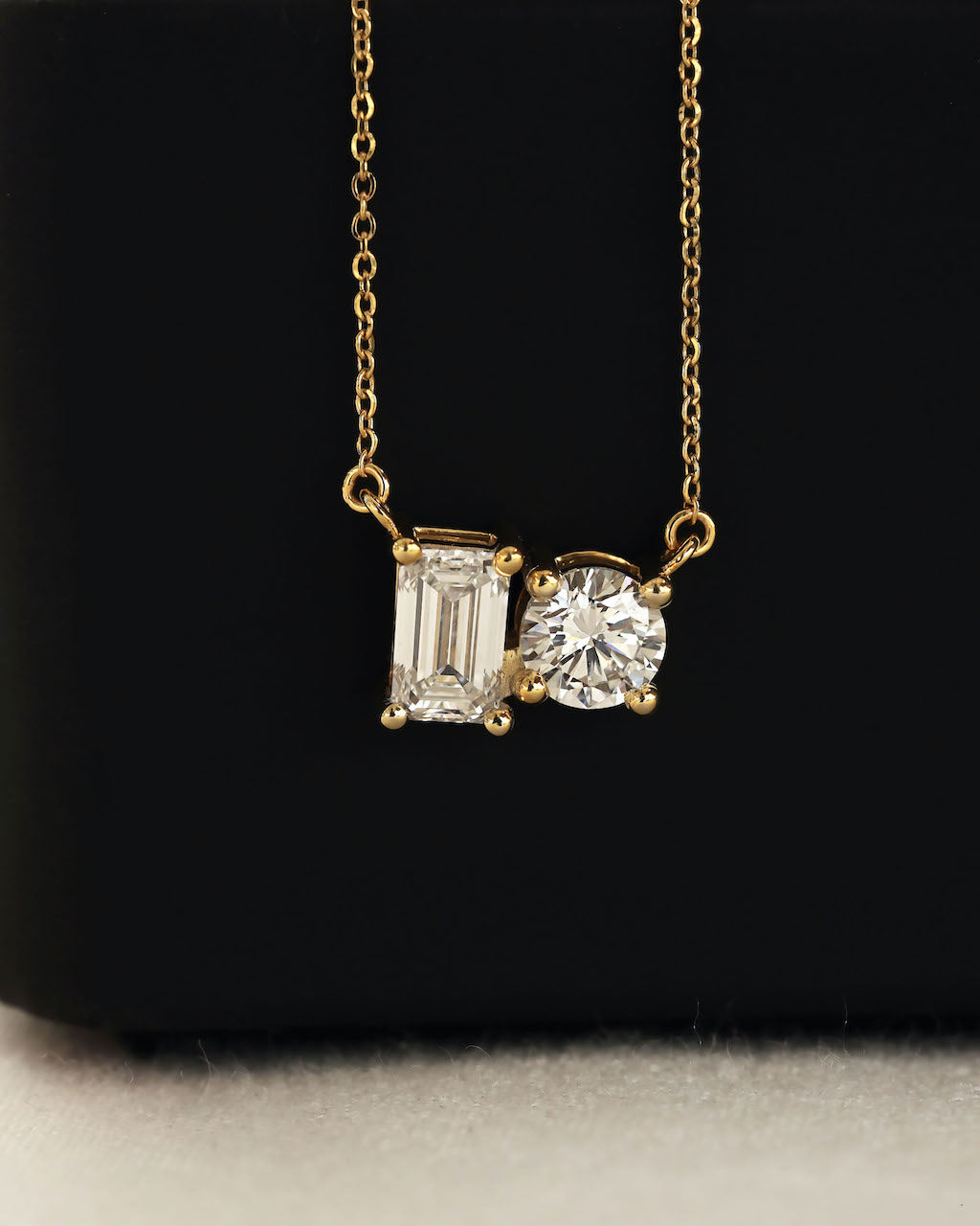 Close up shot of round & emerald cut lab diamond solitaire pendant necklace in yellow gold.
  