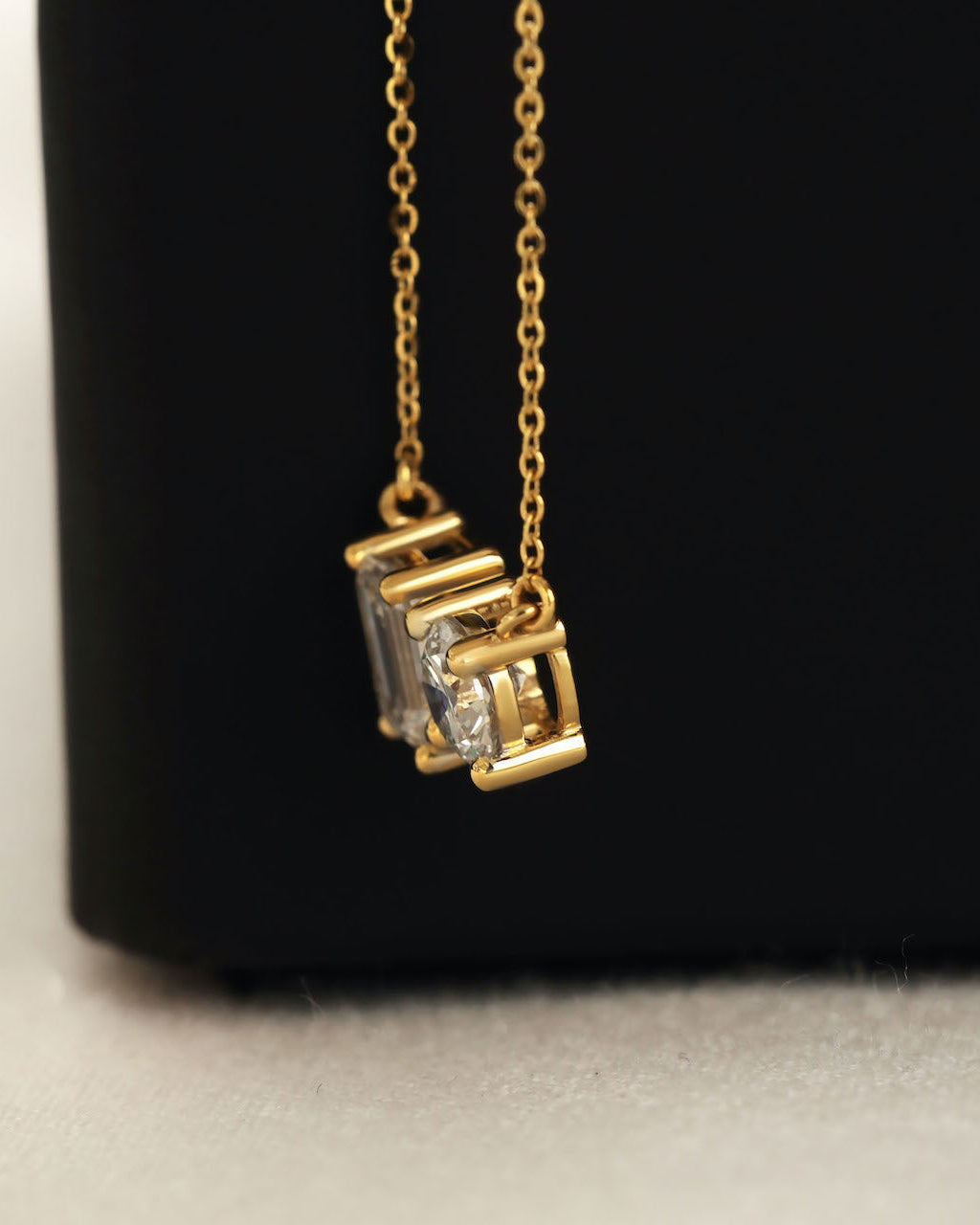 Close up shot of round & emerald cut lab diamond solitaire pendant necklace in yellow gold.
  