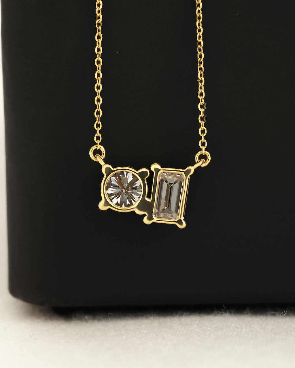 Close up shot of round & emerald cut lab diamond solitaire pendant necklace in yellow gold.
  