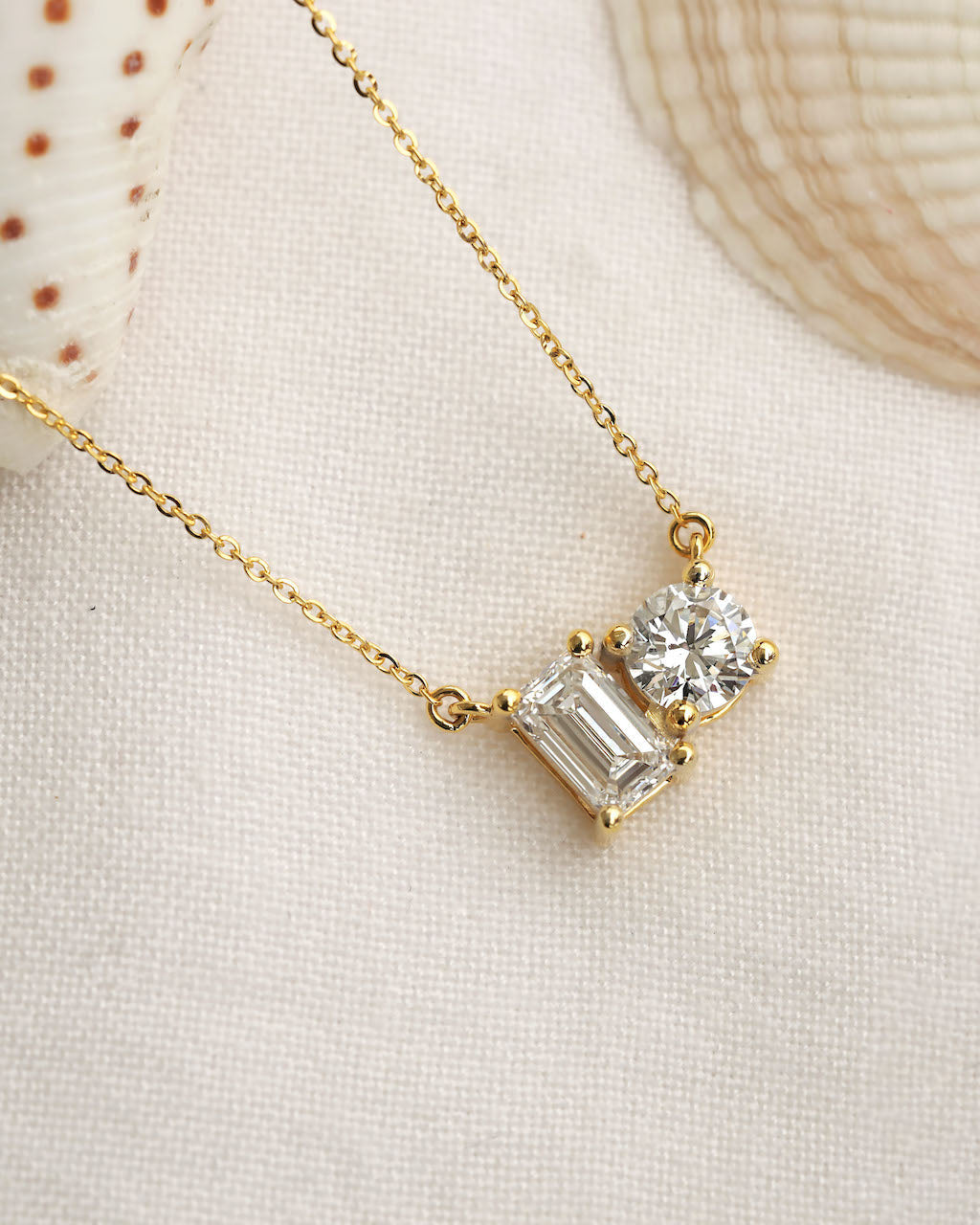 Close up shot of round & emerald cut lab diamond solitaire pendant necklace in yellow gold.
  
