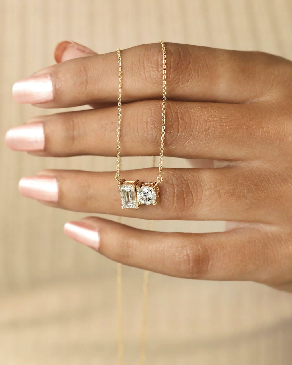 Hand holding round & emerald cut lab diamond solitaire pendant necklace in yellow gold.
  