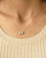 Person wearing round & emerald cut lab diamond solitaire pendant necklace in yellow gold.