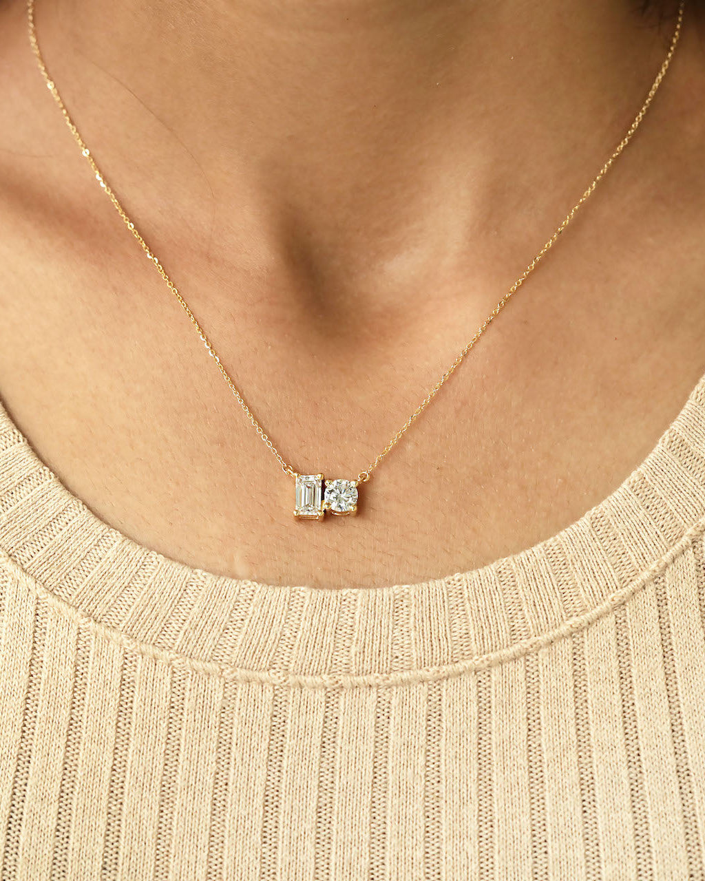 Person wearing round & emerald cut lab diamond solitaire pendant necklace in yellow gold.